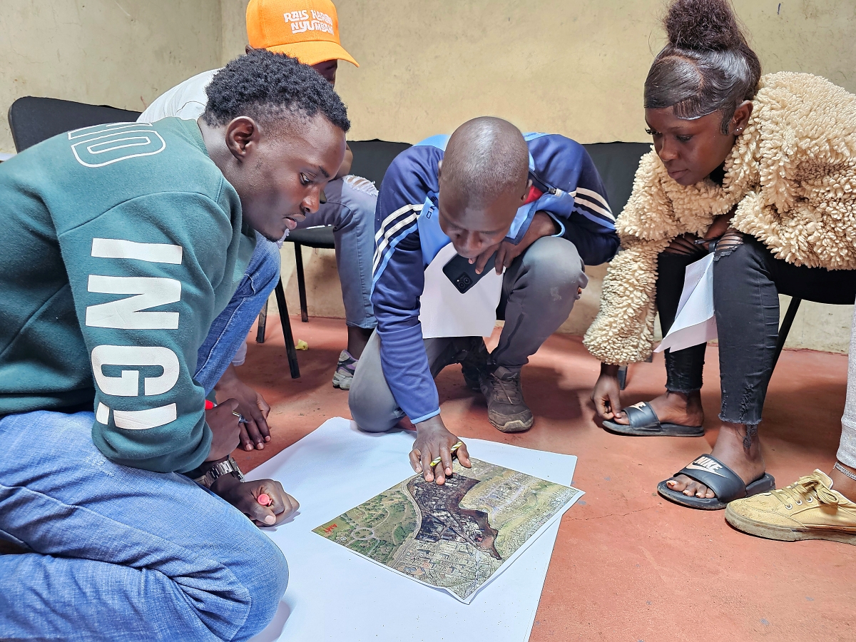 A group of participants gathers around a printed aerial map on the floor during a discussion.